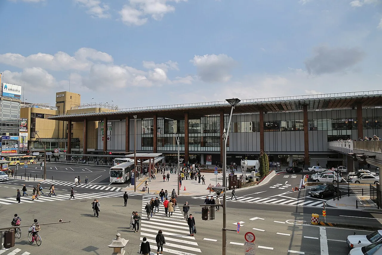 Nagano Station's glass front behind tall wooden pillars, with buses, taxis and a busy crossing in front