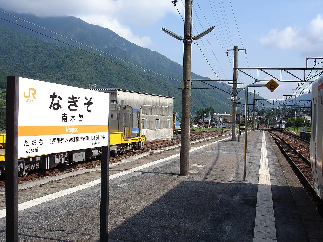The platform at JR Nagiso Station, with the station sign and wooded mountains behind