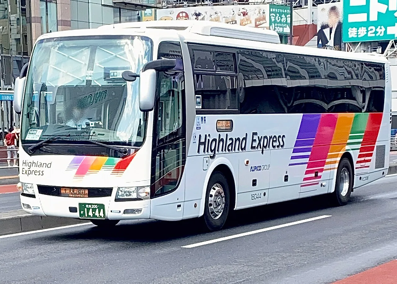 A white Alpico Highland Express coach with rainbow stripes on a city street