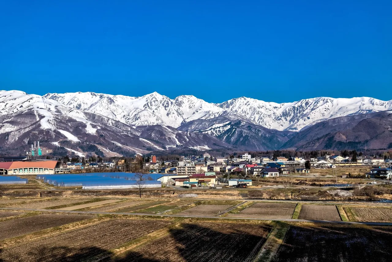 Snow-covered Hakuba mountains above the houses and bare fields of Hakuba village in April