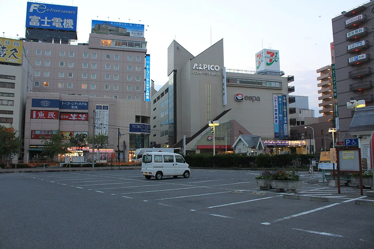 The Alpico bus terminal building in Matsumoto, seen across an open car park in the evening