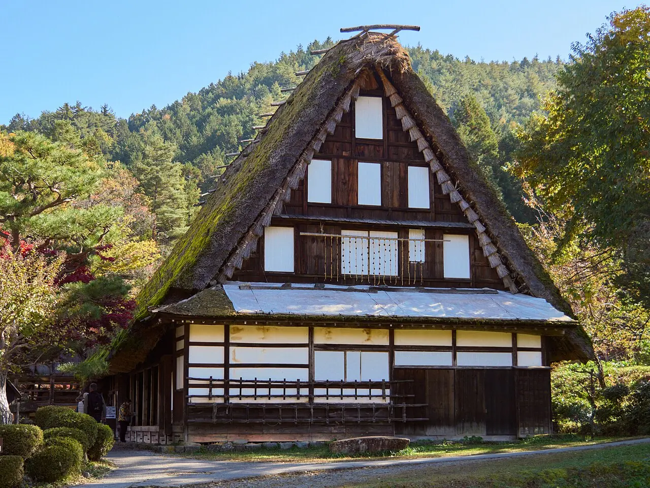 A steep thatched-roof farmhouse at Hida Folk Village under a blue sky in November